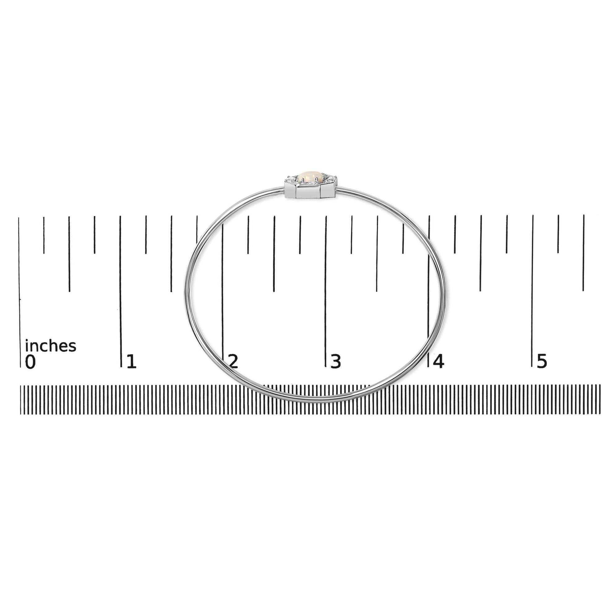 White metal bracelet with a central round white opal gemstone surrounded by round and baguette white gemstones, shown flat on a ruler for scale, top-down view.