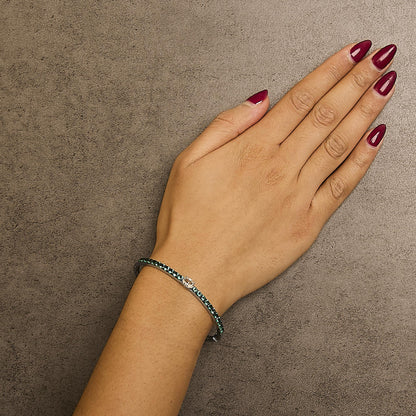 White metal bracelet with round green gemstones and one oval white gemstone, shown worn on a model's wrist from a top angle.