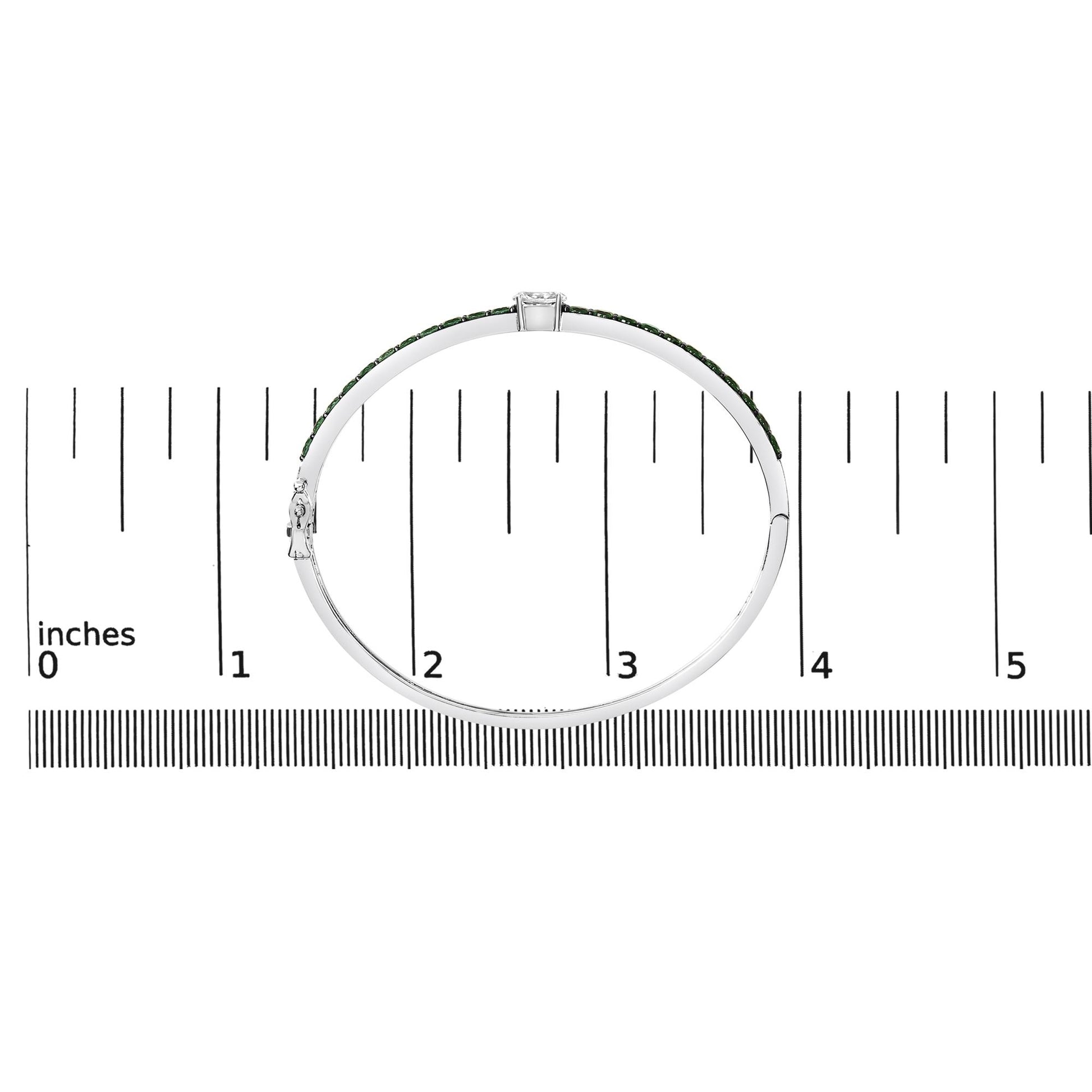 White metal bracelet with a row of round green gemstones and one oval white gemstone in a prong setting, shown on a ruler scale from side angle.