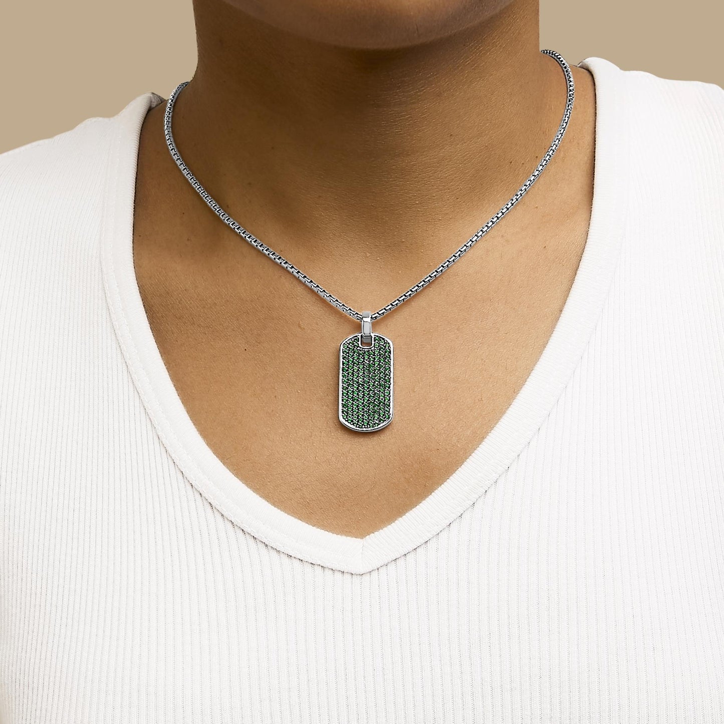 Necklace with a rectangular white metal pendant encrusted with round green gemstones in a shared prong setting, shown worn on a model from a front angle.