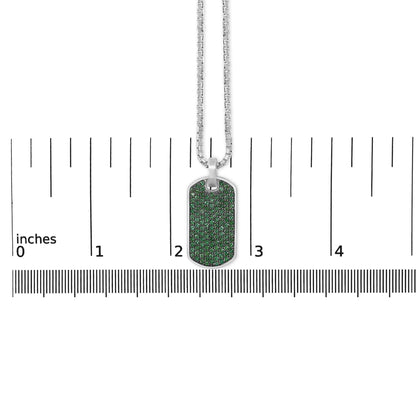 Close-up front view of a white metal dog tag style necklace pendant with round green gemstones set in a shared prong setting, shown on a scale.