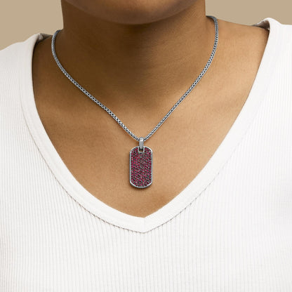 Necklace with a white metal rectangular pendant covered in round red gemstones in a shared prong setting, shown worn on a model from a front angle.