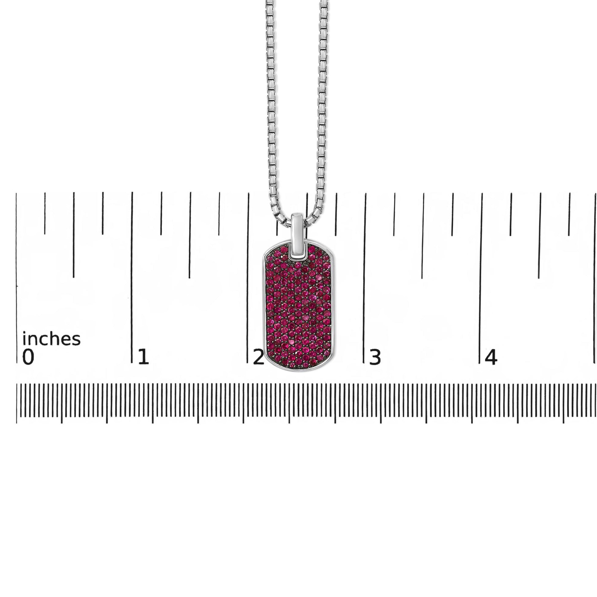 Front-facing close-up of a white metal necklace with a rectangular pendant encrusted with round red gemstones, shown on a ruler scale.