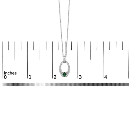White metal necklace with an oval-shaped green gemstone center set in a prong setting, surrounded by multiple round white gemstones, shown on a ruler scale from a front angle.