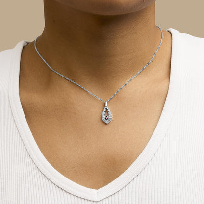 Close-up frontal view of a white metal necklace with a teardrop-shaped pendant shown worn on a model. The pendant features a central red princess-shaped gemstone surrounded by small round white gemstones.