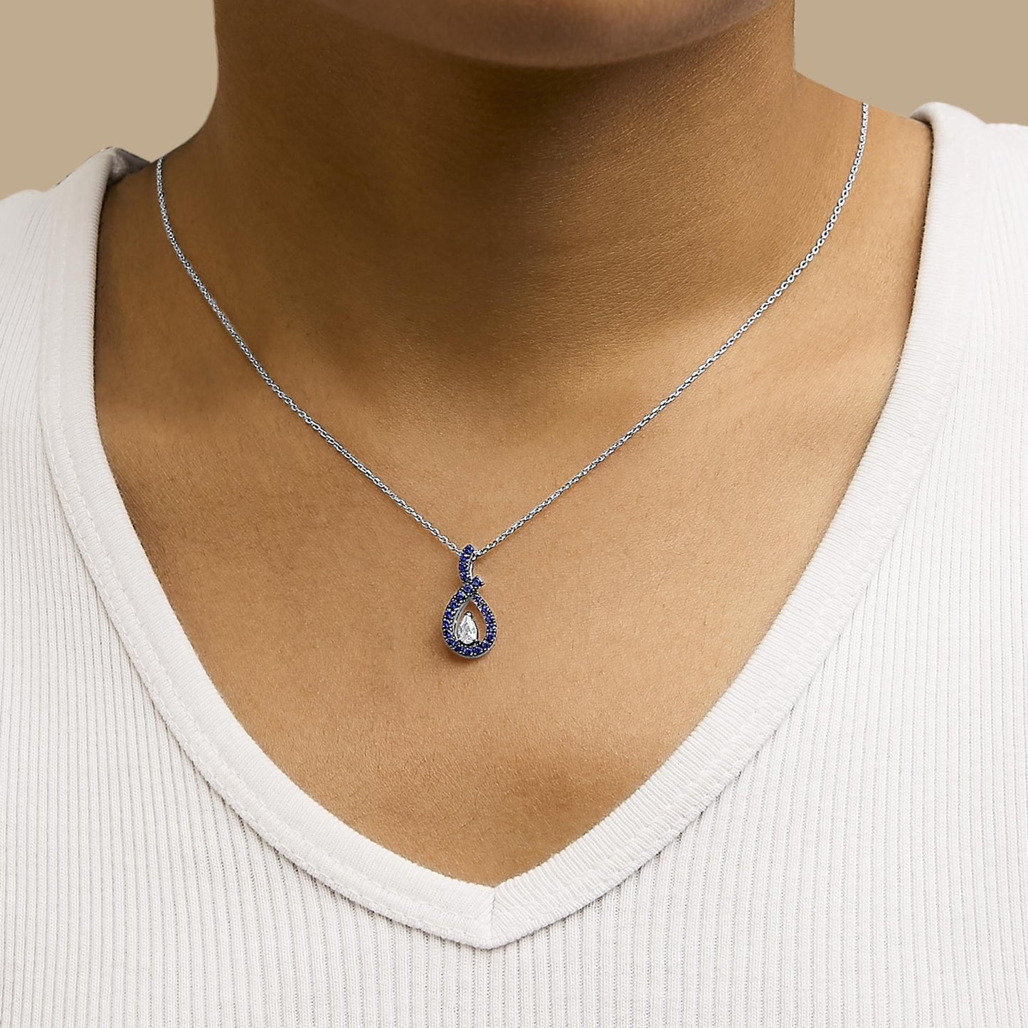 White metal necklace with a pear-shaped white gemstone pendant surrounded by round blue gemstones, shown worn on a model from a front angle.