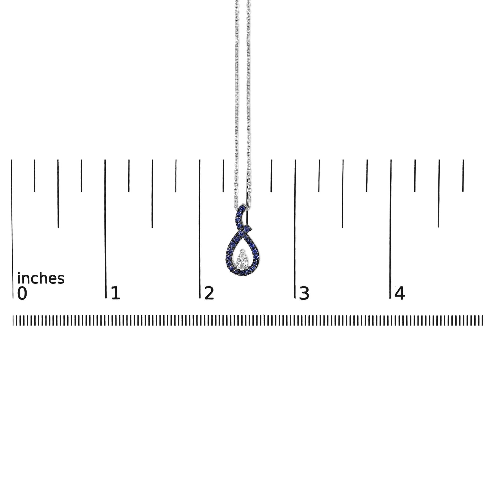 White metal necklace with a loop-shaped pendant featuring a central pear-shaped white gemstone surrounded by round blue gemstones, shown on a scale from a front angle.
