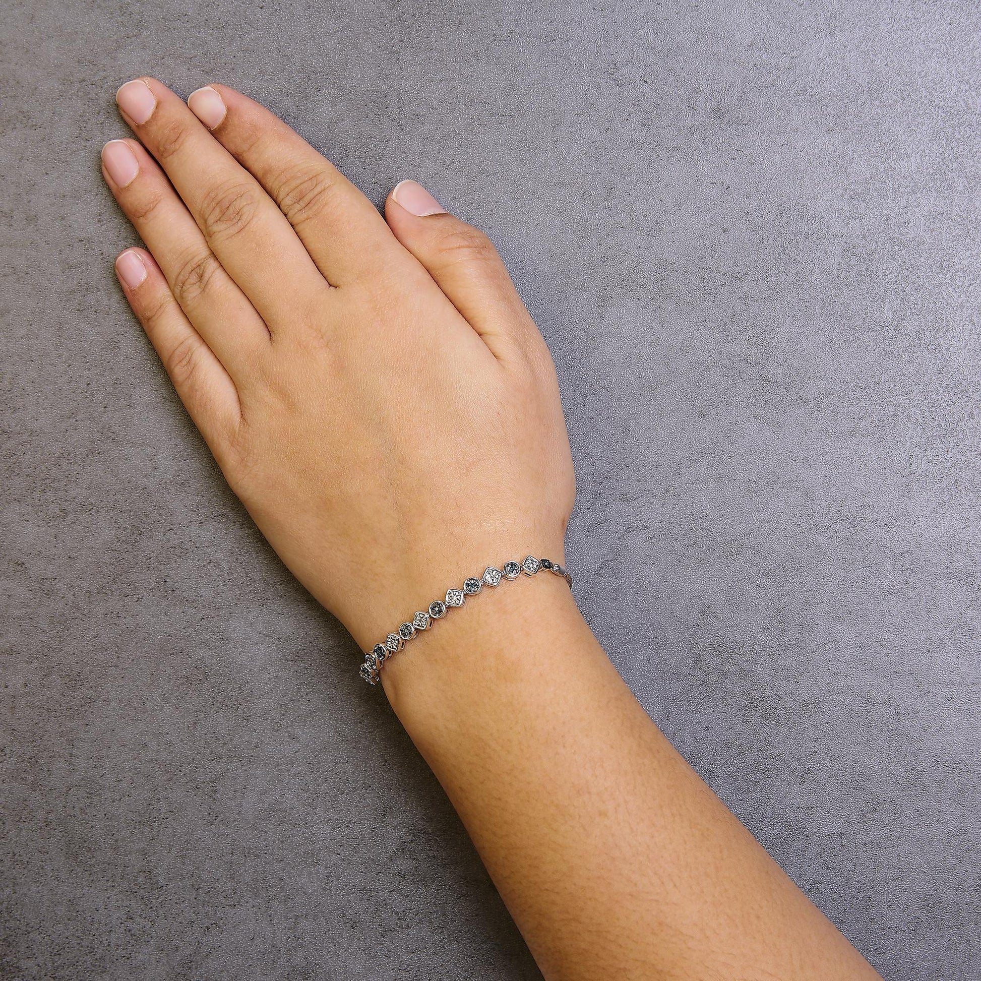 White metal bracelet with alternating white and blue round gemstones in miracle settings, worn on model's wrist, top-down angle.