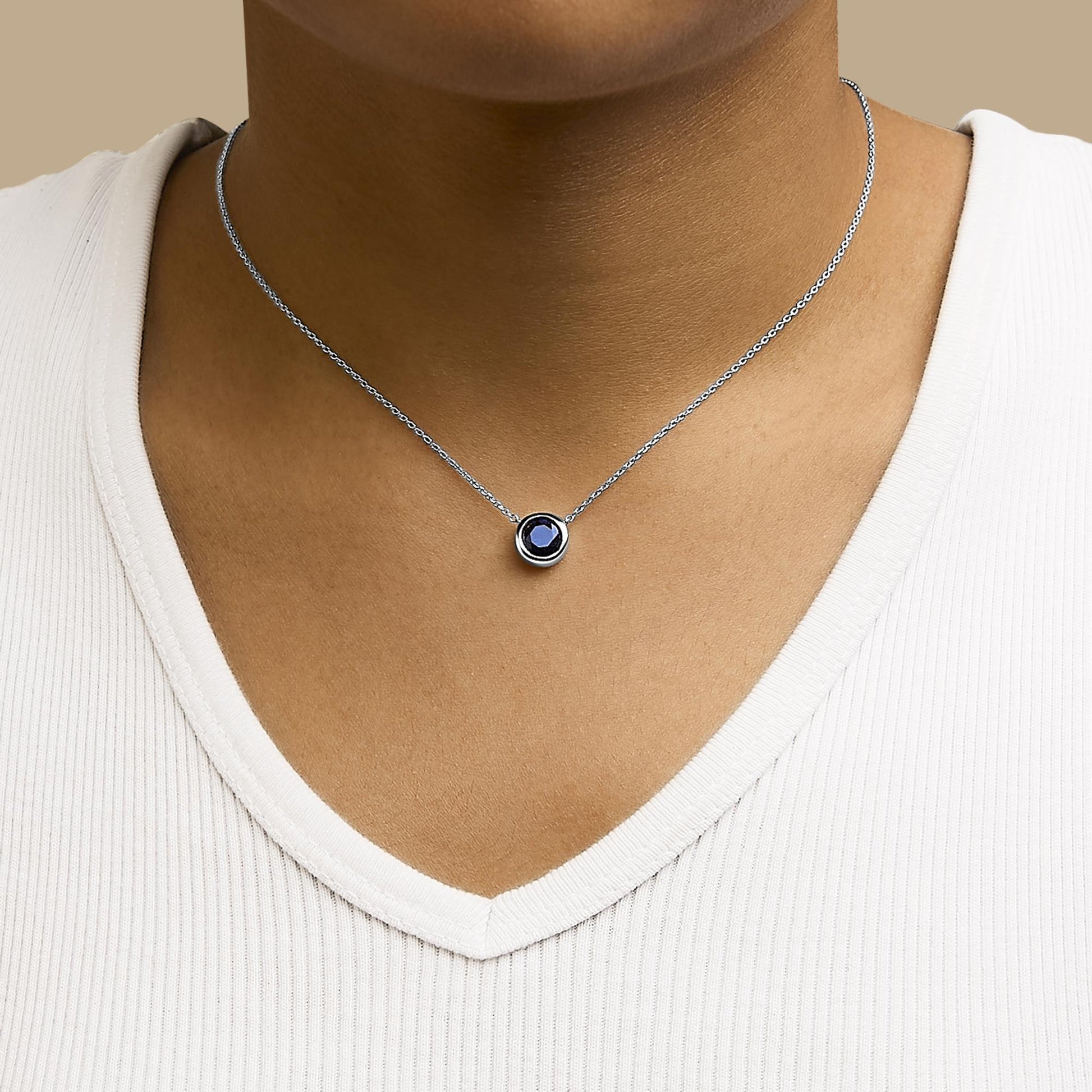 White metal necklace with a round blue gemstone in a bezel setting, shown worn on a model from the front angle.