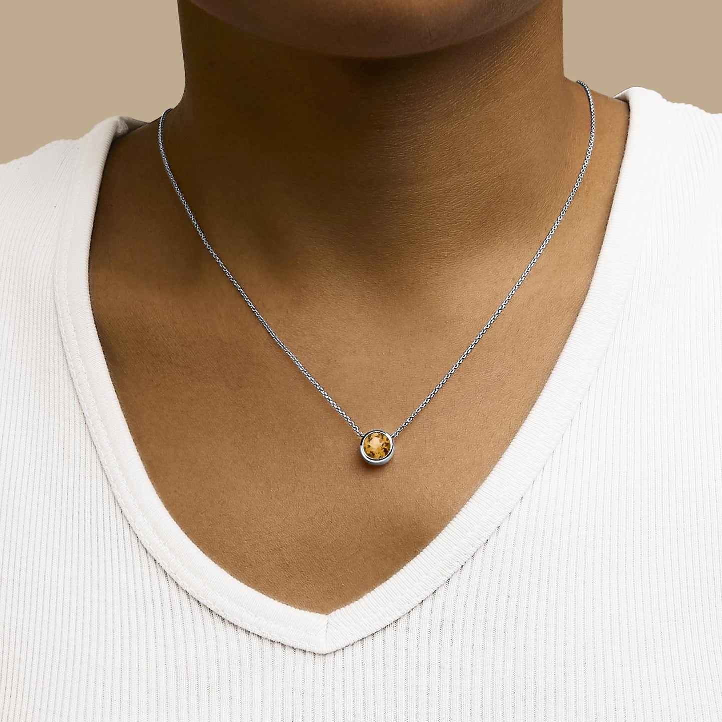 White necklace with a round yellow gemstone in bezel setting, shown worn on a model, front view.