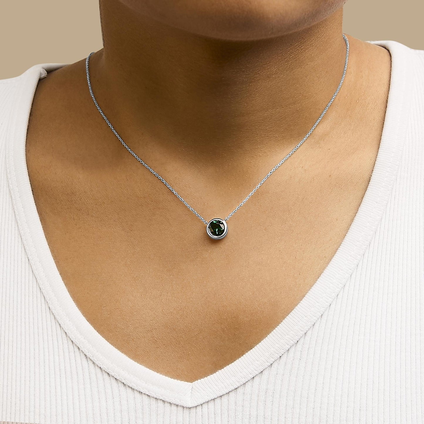 White necklace with a round green gemstone in bezel setting, shown worn on a model from the front angle.