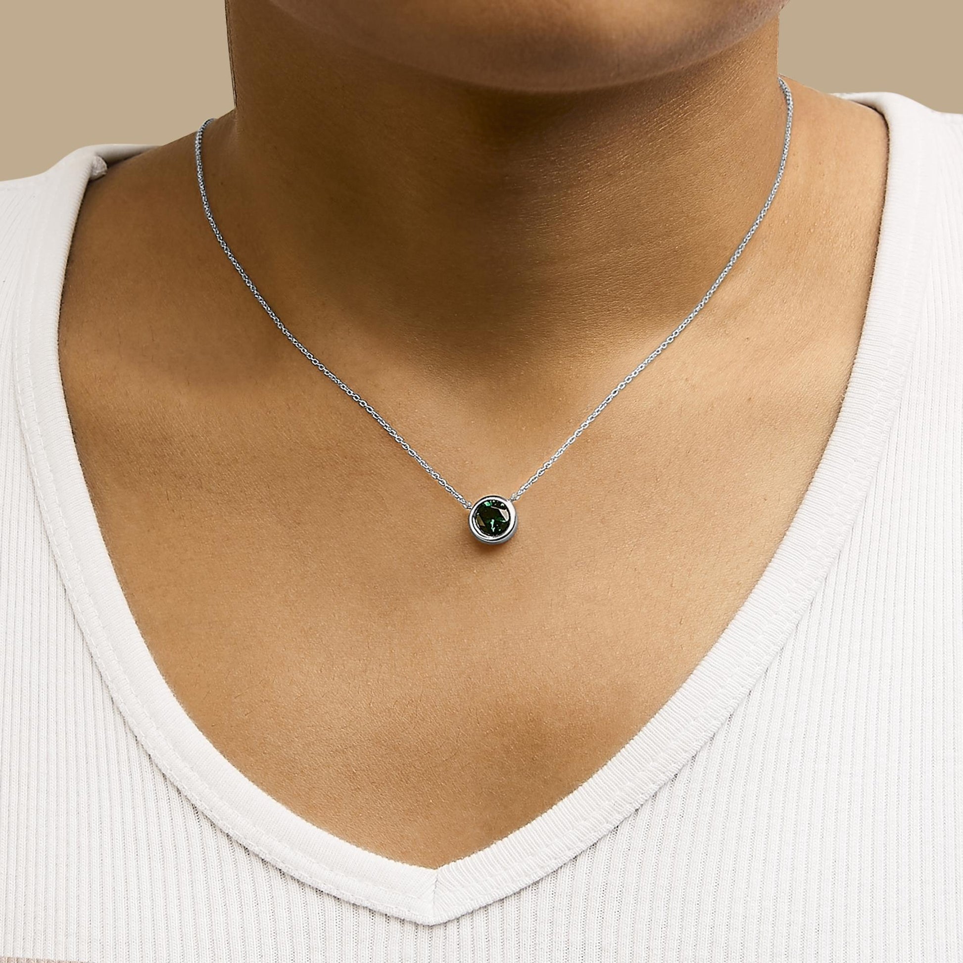 White necklace with a round green gemstone in bezel setting, shown worn on a model from the front angle.