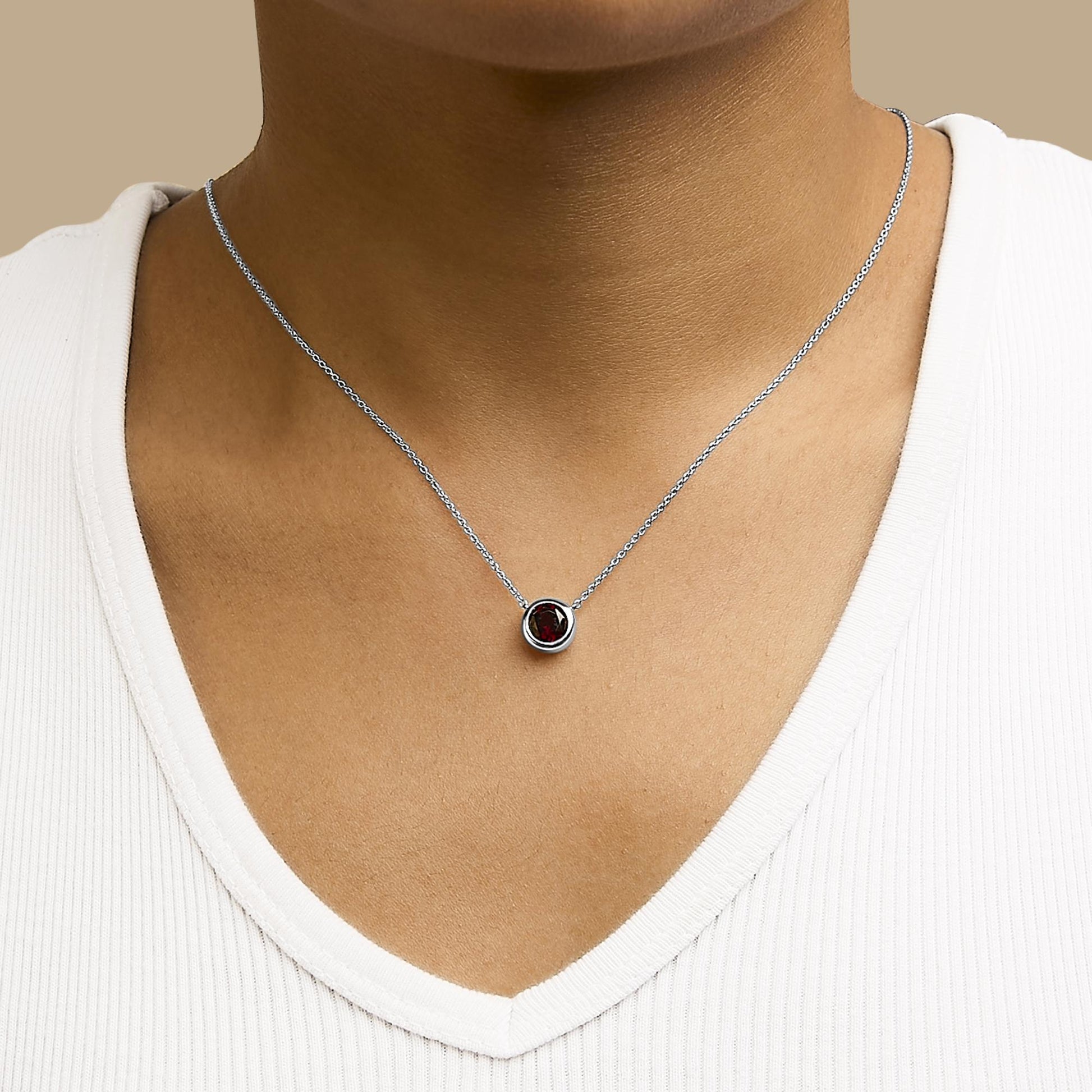 Necklace with a small round red gemstone in a bezel setting on a delicate white chain, shown worn on a model from the front.
