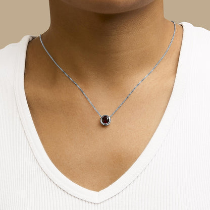 Necklace with a small round red gemstone in a bezel setting on a delicate white chain, shown worn on a model from the front.