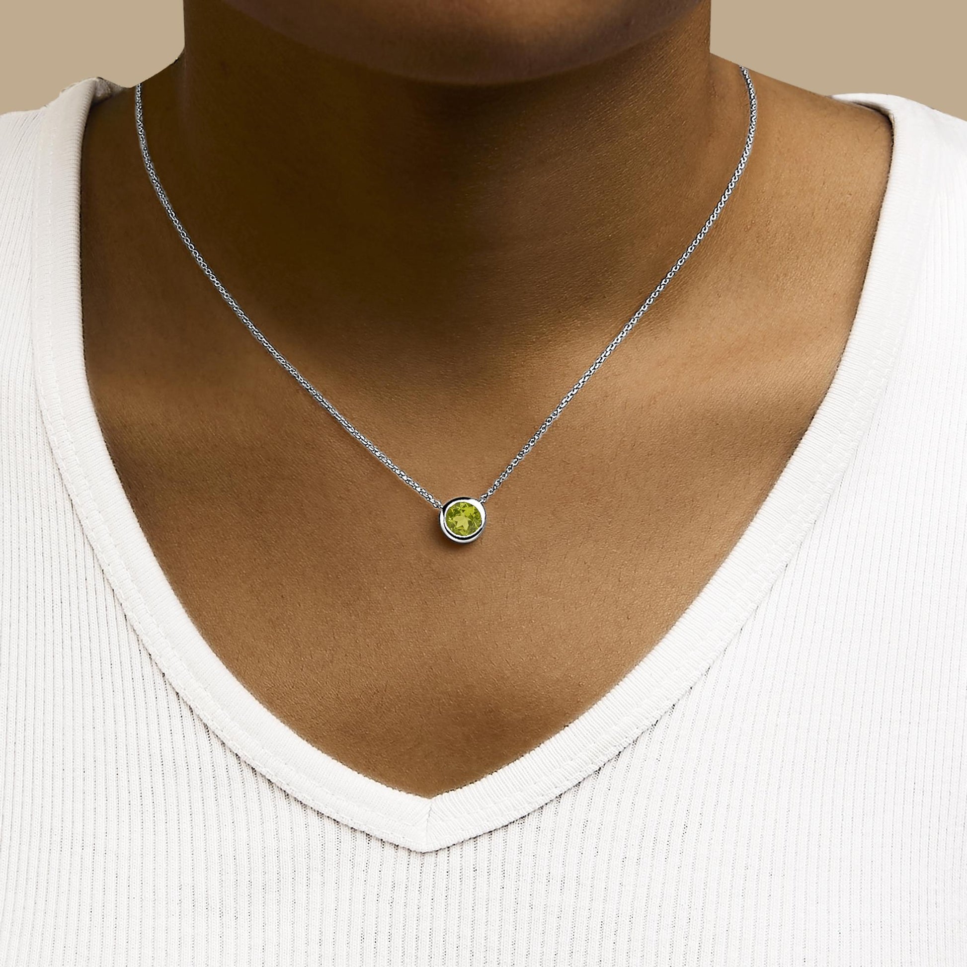 Necklace with a round green gemstone in bezel setting on a white chain, shown worn on a model from the front.