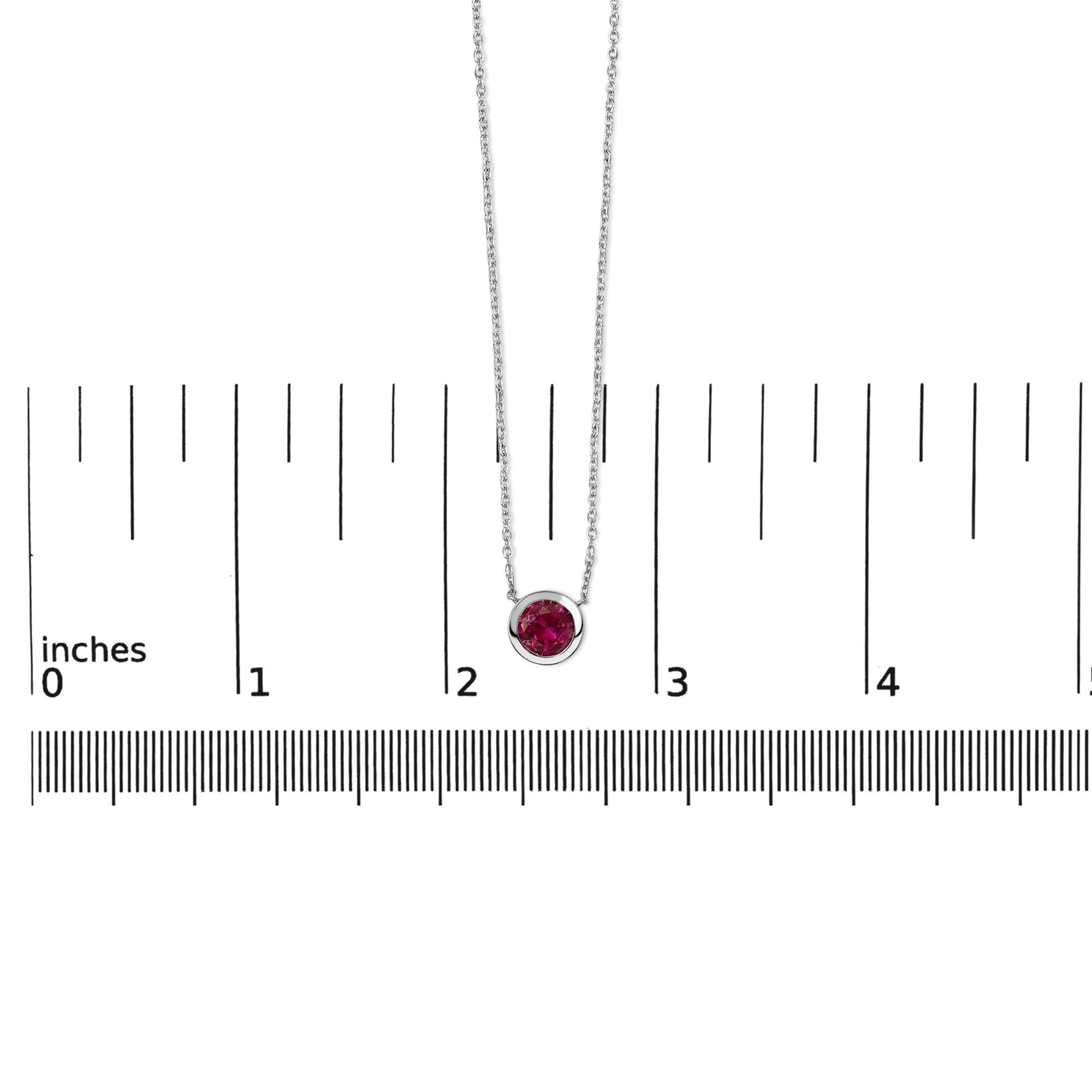 White necklace with a round red gemstone in a bezel setting, shown on a scale with a front-facing angle.