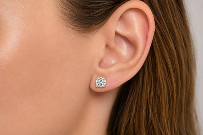 Close-up side view of a model's ear wearing a yellow metal stud earring with a round white gemstone in a four-prong setting.