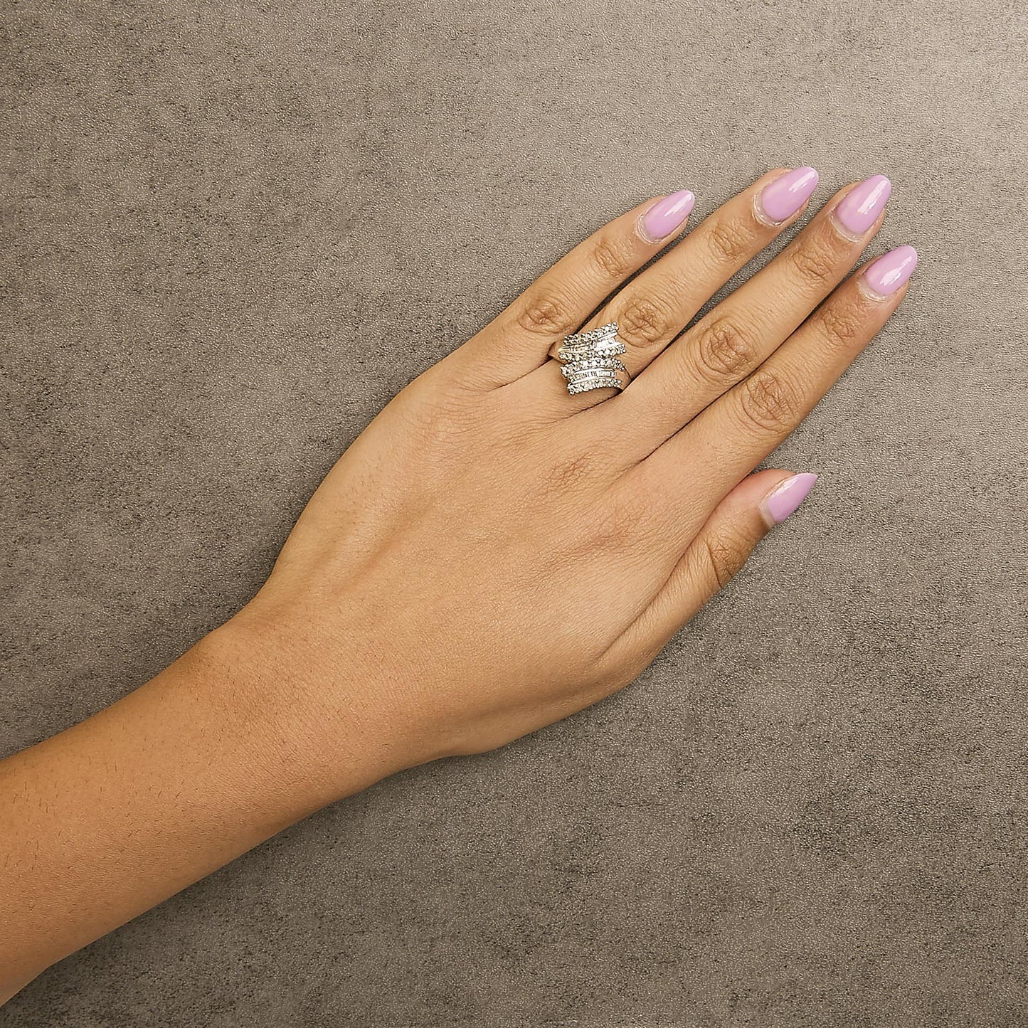 White metal ring with round white gemstones in prong setting and baguette white gemstones in channel setting, shown worn on a model's hand, top view.