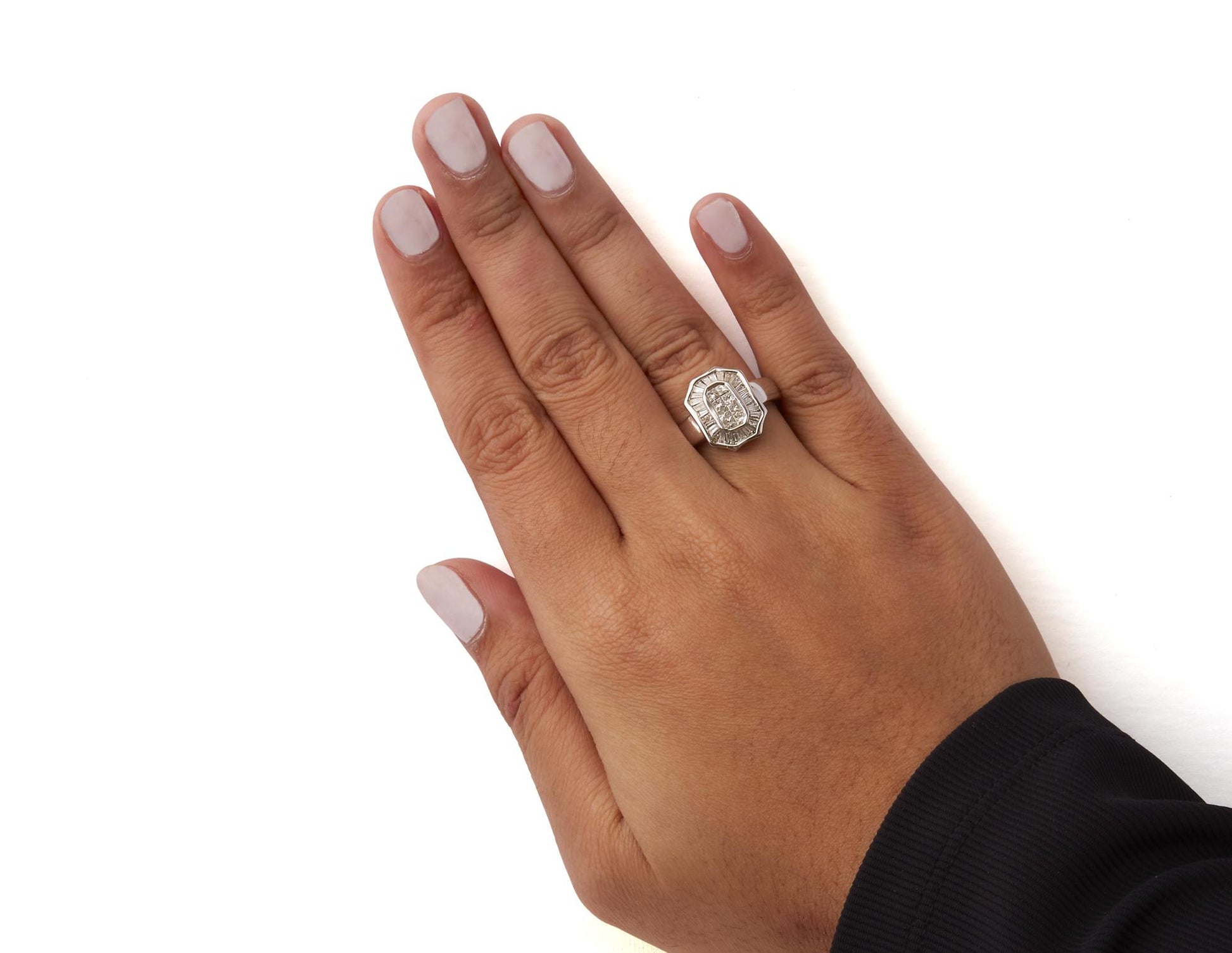 Close-up top view of a hand wearing a white metal ring featuring white baguette-shaped gemstones in a channel setting and white princess-shaped gemstones in an invisible setting.
