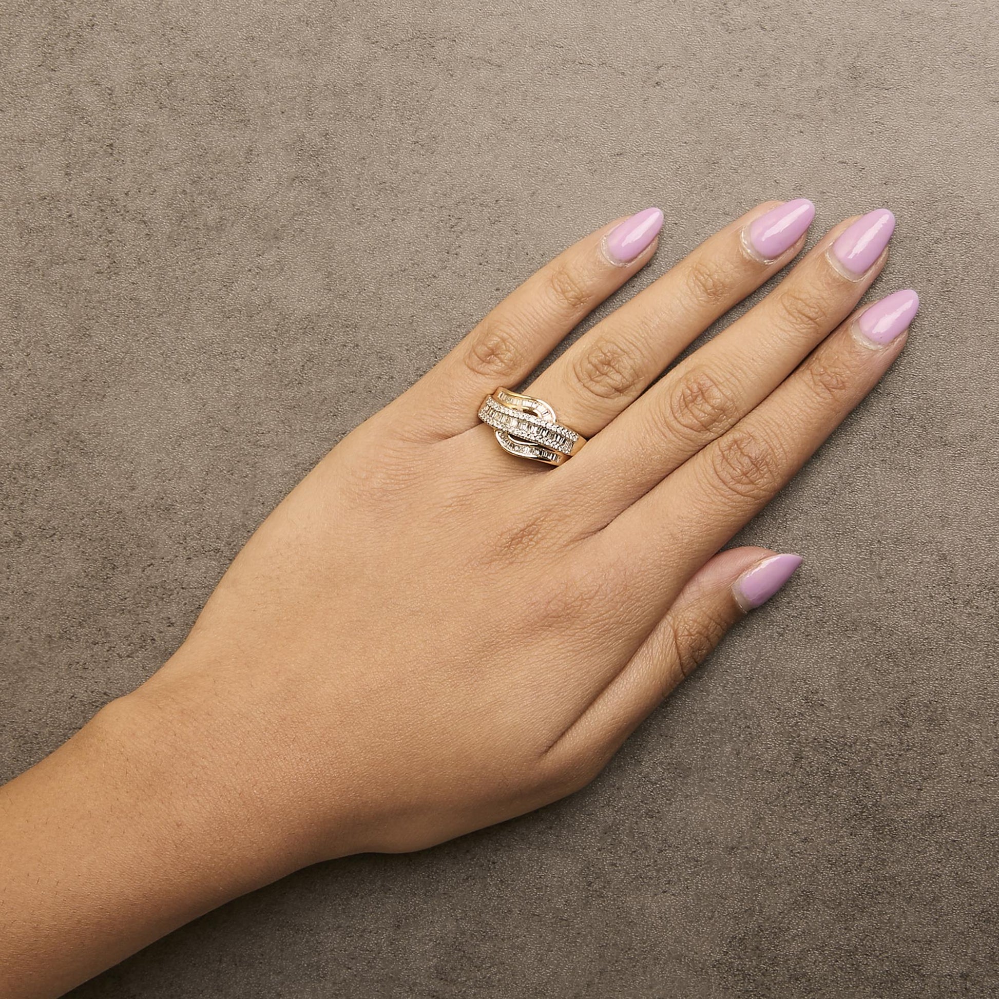Yellow metal ring with intertwined bands featuring round white gemstones in prong settings and baguette white gemstones in channel settings, shown worn on a model's hand from an overhead angle.