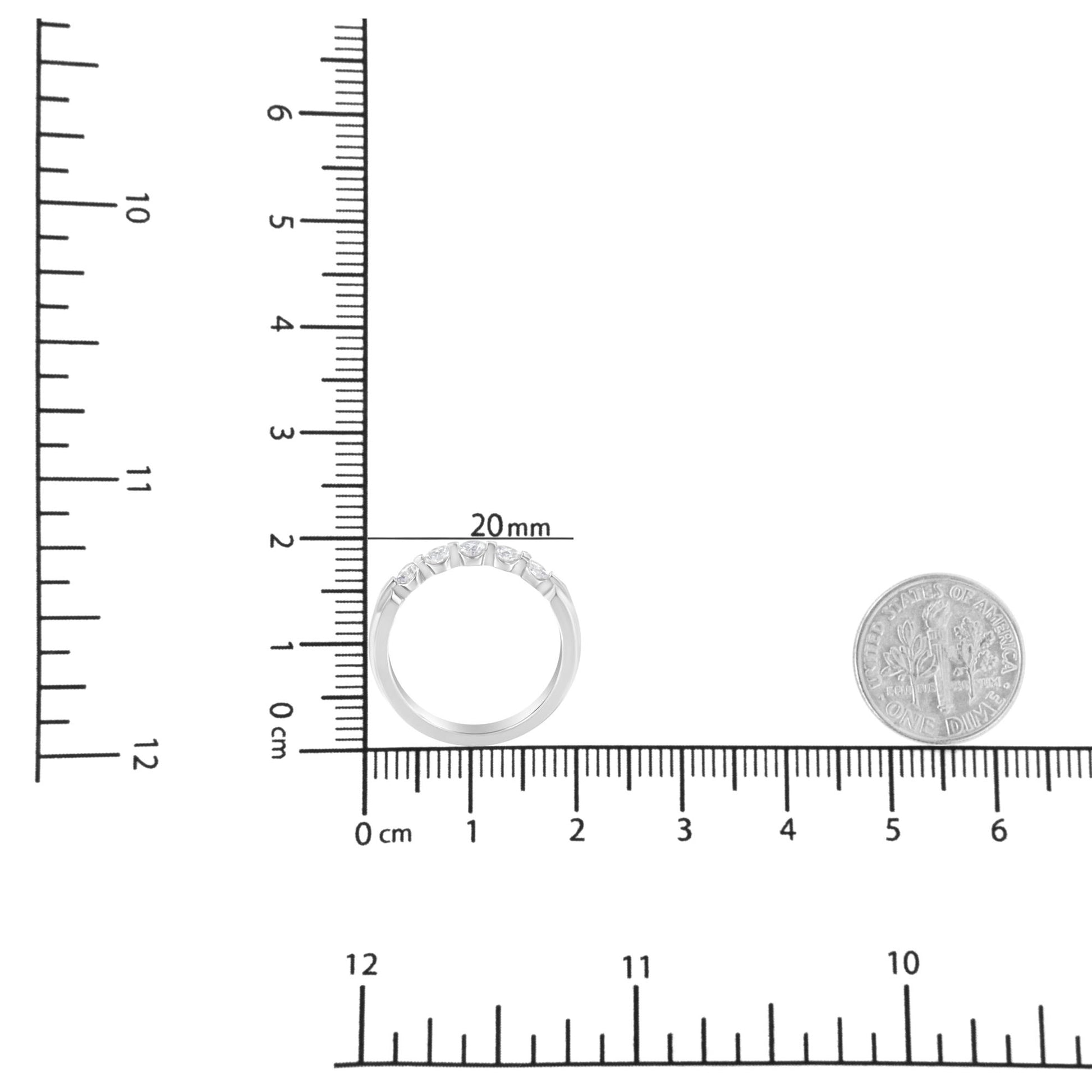 White metal ring with five round white gemstones in a channel setting, shown from the top on a ruler and next to a coin for size reference.