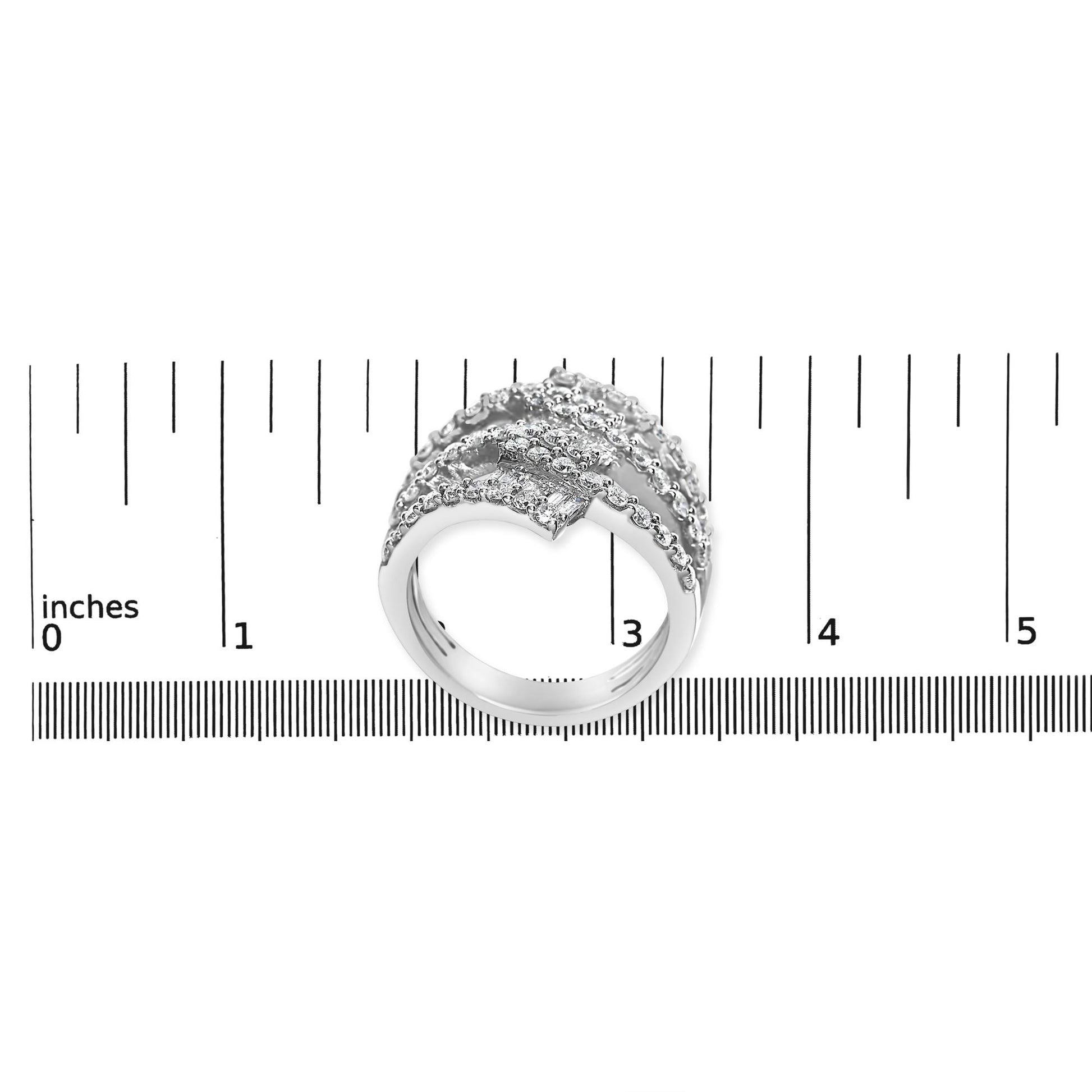 White metal ring with rows of round and baguette-shaped white gemstones in prong and channel settings, shown from a top angle on a ruler scale.