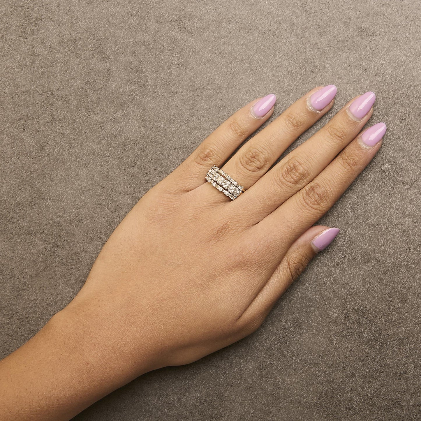 Yellow metal ring with rows of round white gemstones in prong settings and baguette white gemstones in channel settings, shown worn on a model's finger from a top angle.