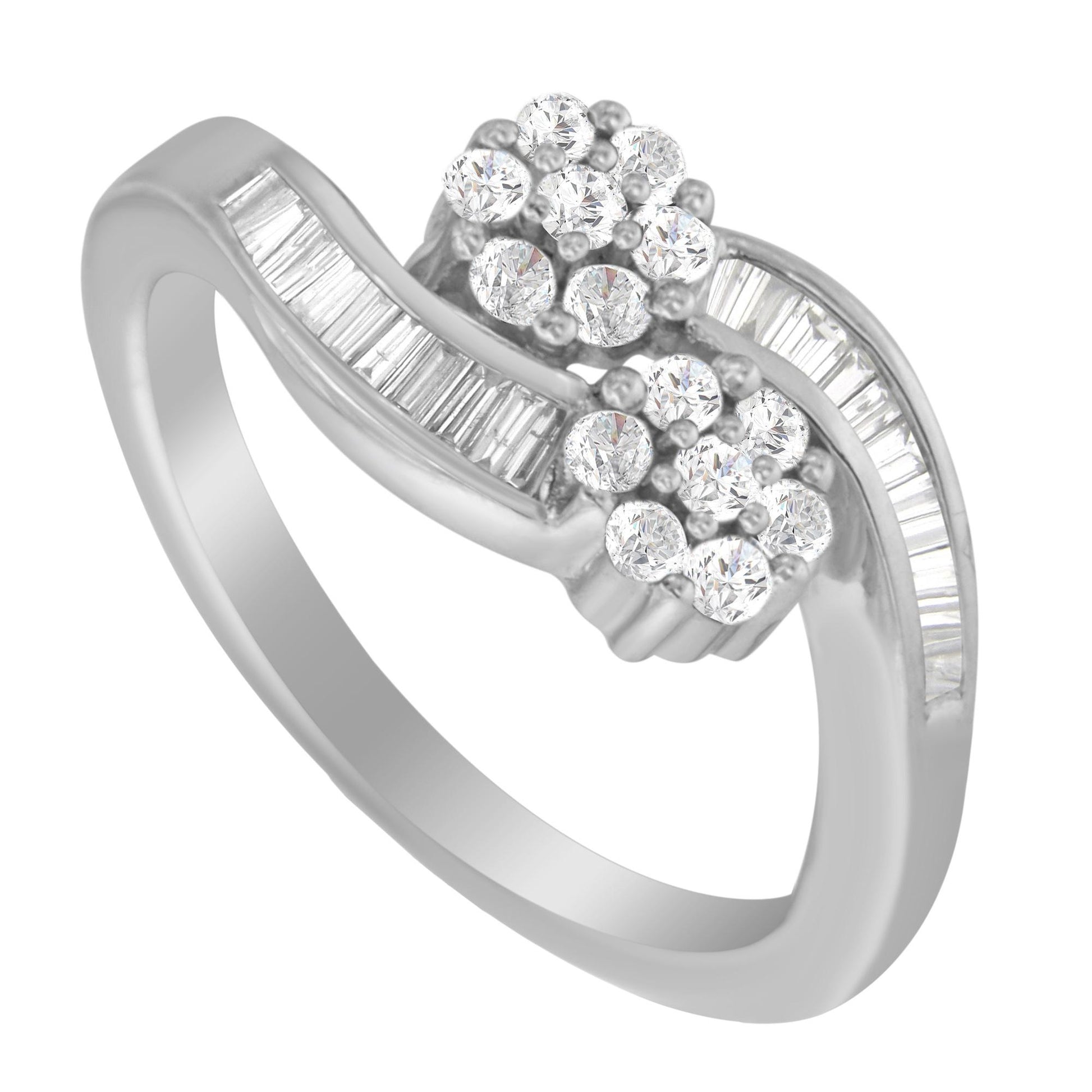 White metal ring with a wavy design featuring clusters of round white gemstones in prong settings and baguette-shaped white gemstones in channel settings, shown at an angled close-up.