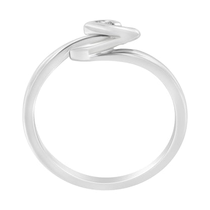 White metal ring viewed from the side with a round white gemstone in bezel setting and a zigzag design.
