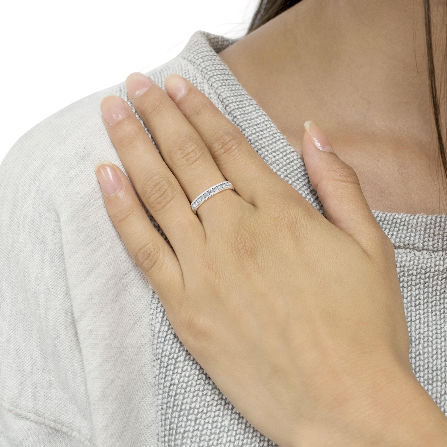 White metal ring with channel-set round white gemstones, worn on a model's finger, shot from an angled top view.
