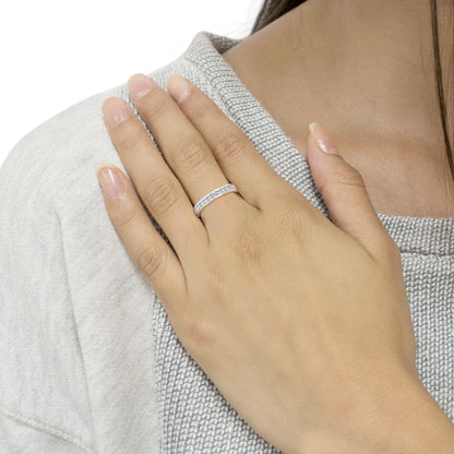 White metal ring with channel-set round white gemstones, worn on a model's finger, shot from an angled top view.