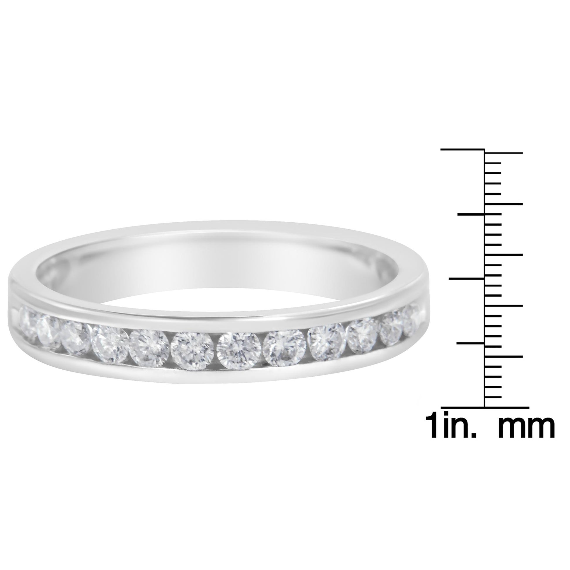 Close-up front view of a white metal ring with round white gemstones in a channel setting, shown next to a ruler for size reference.