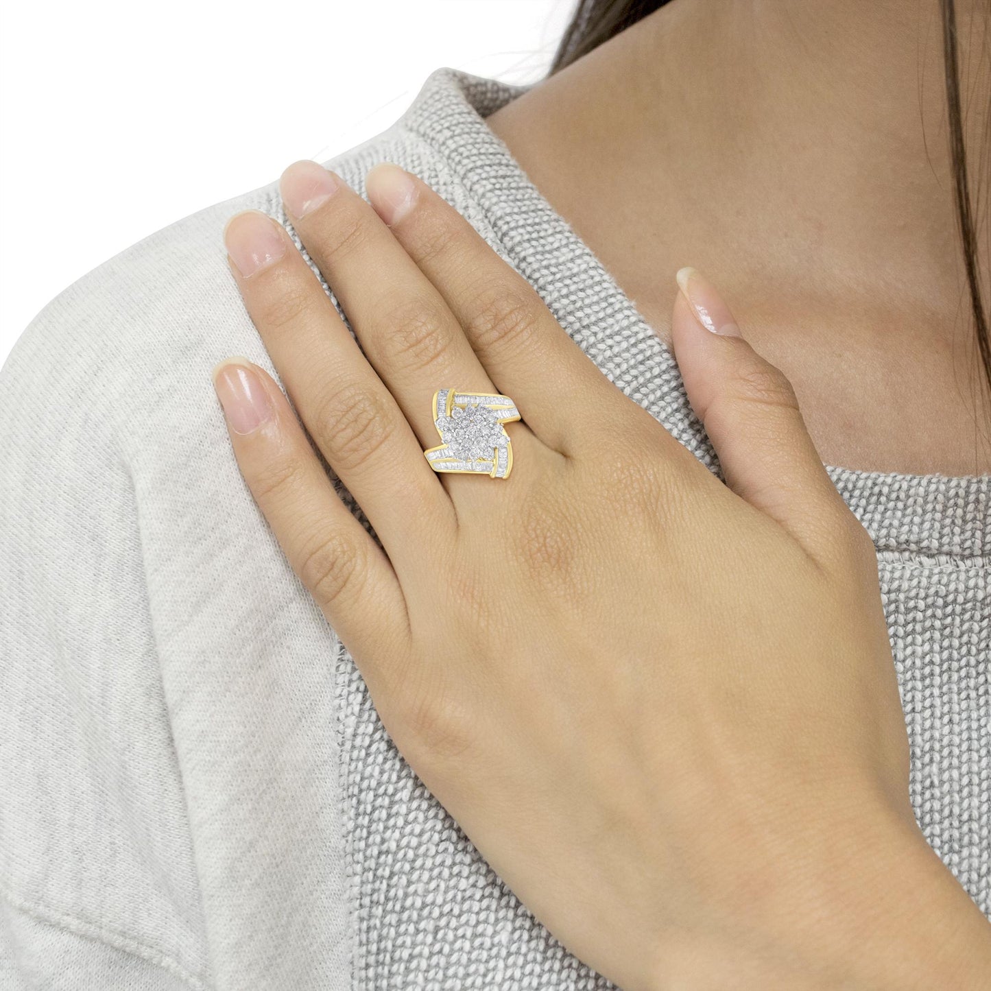 Yellow metal ring with round white gemstones in prong setting at center and baguette white gemstones in channel setting on sides, worn on a model’s finger, angled top view.