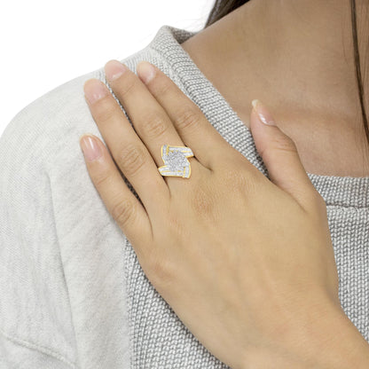Yellow metal ring with round white gemstones in prong setting at center and baguette white gemstones in channel setting on sides, worn on a model’s finger, angled top view.