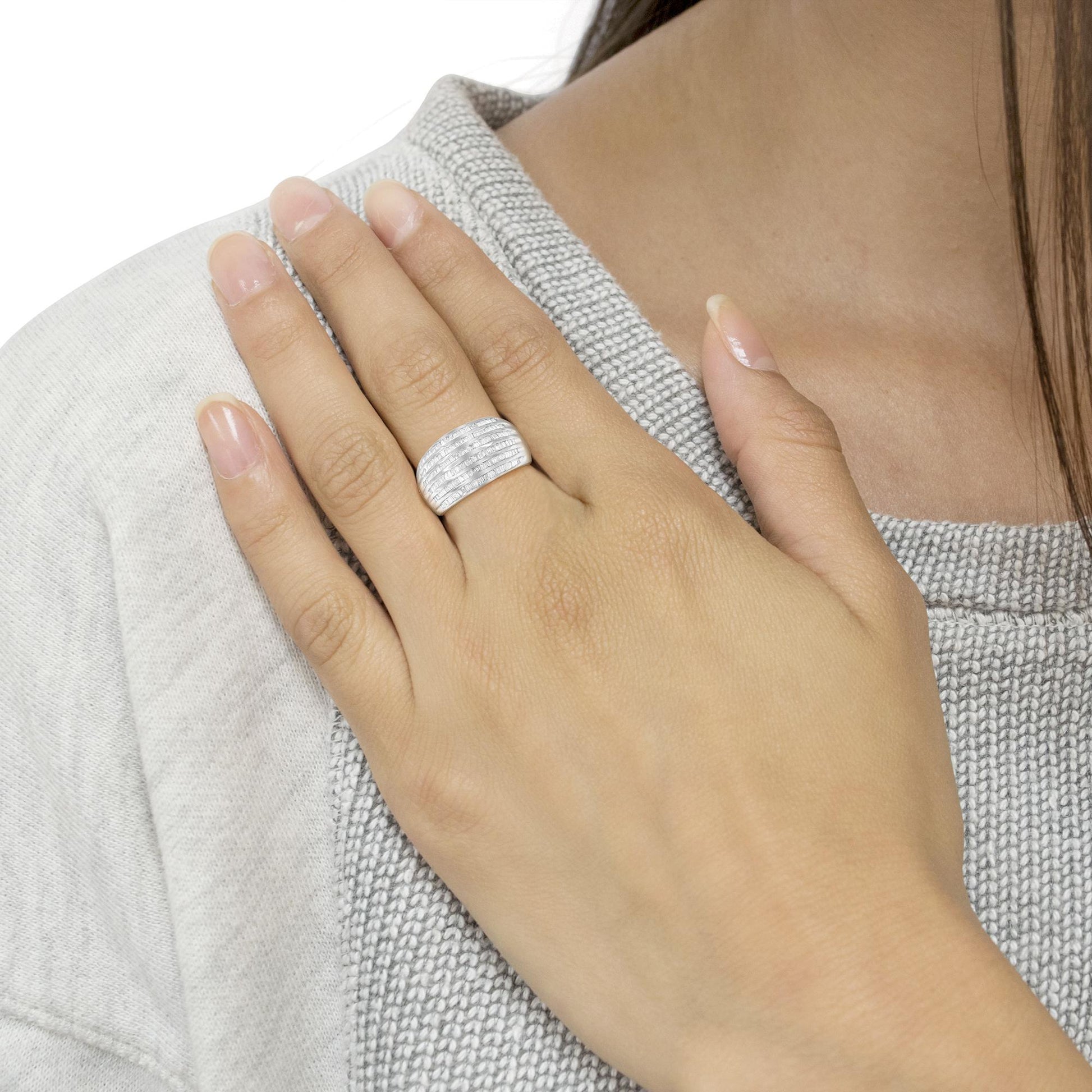 Close-up of a white metal ring with multiple rows of baguette-shaped white gemstones in a channel setting, worn on a model's finger, angled slightly from above.
