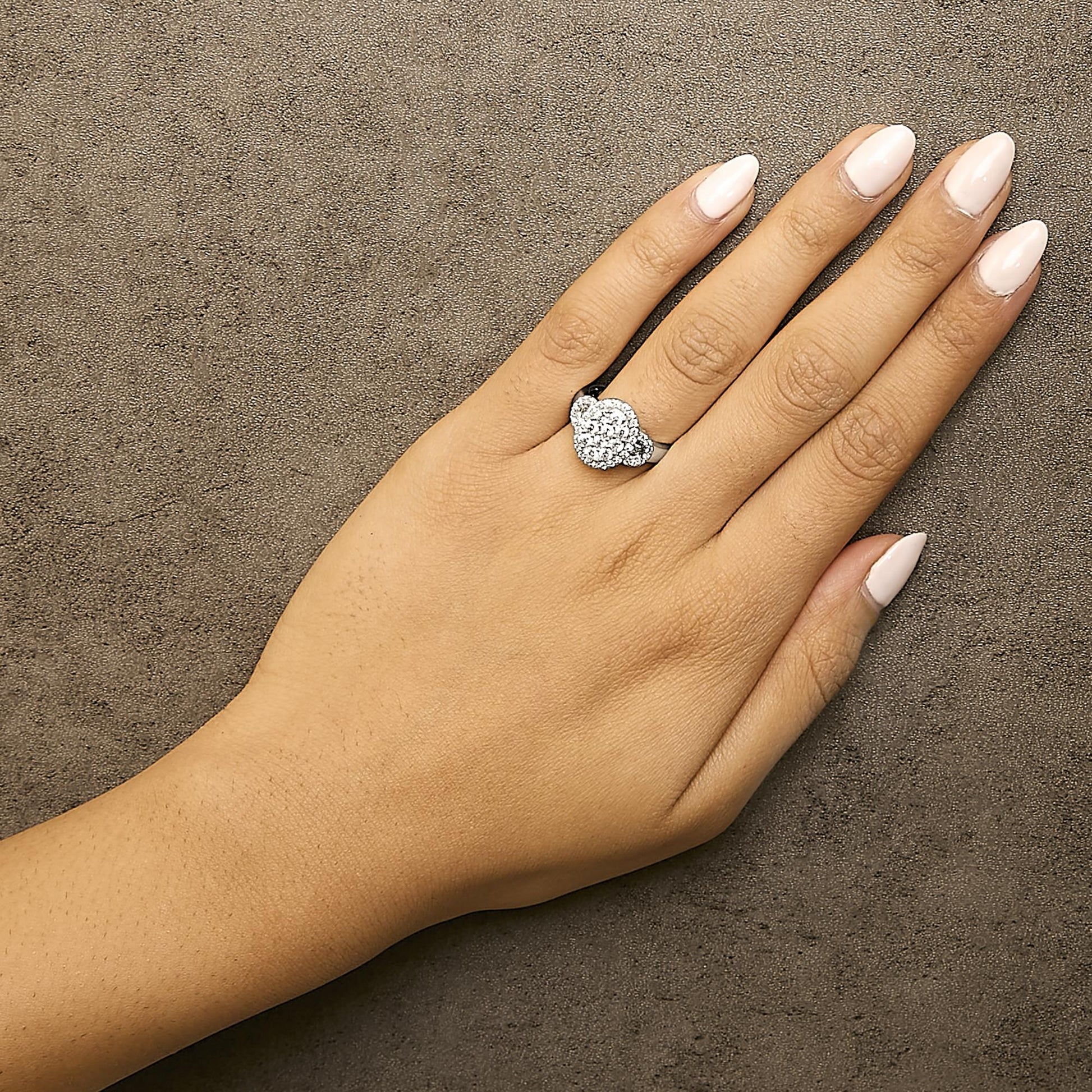 White metal ring with clusters of round and baguette white gemstones in prong and channel settings, shown on a model's hand from above.