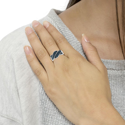 White metal ring with twisting design accented with round blue gemstones in prong settings, shown on a model's hand angled across the chest.