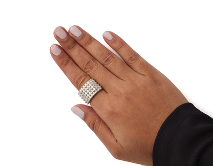 White metal wide band ring with multiple rows of round white gemstones in prong settings, shown worn on a model's hand from a top angle.