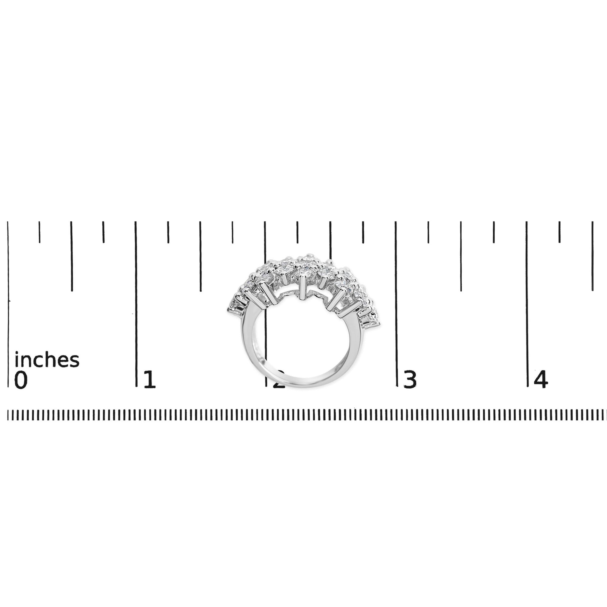 White metal ring with multiple round white gemstones in prong settings, shown from a front angle on a ruler for size reference.