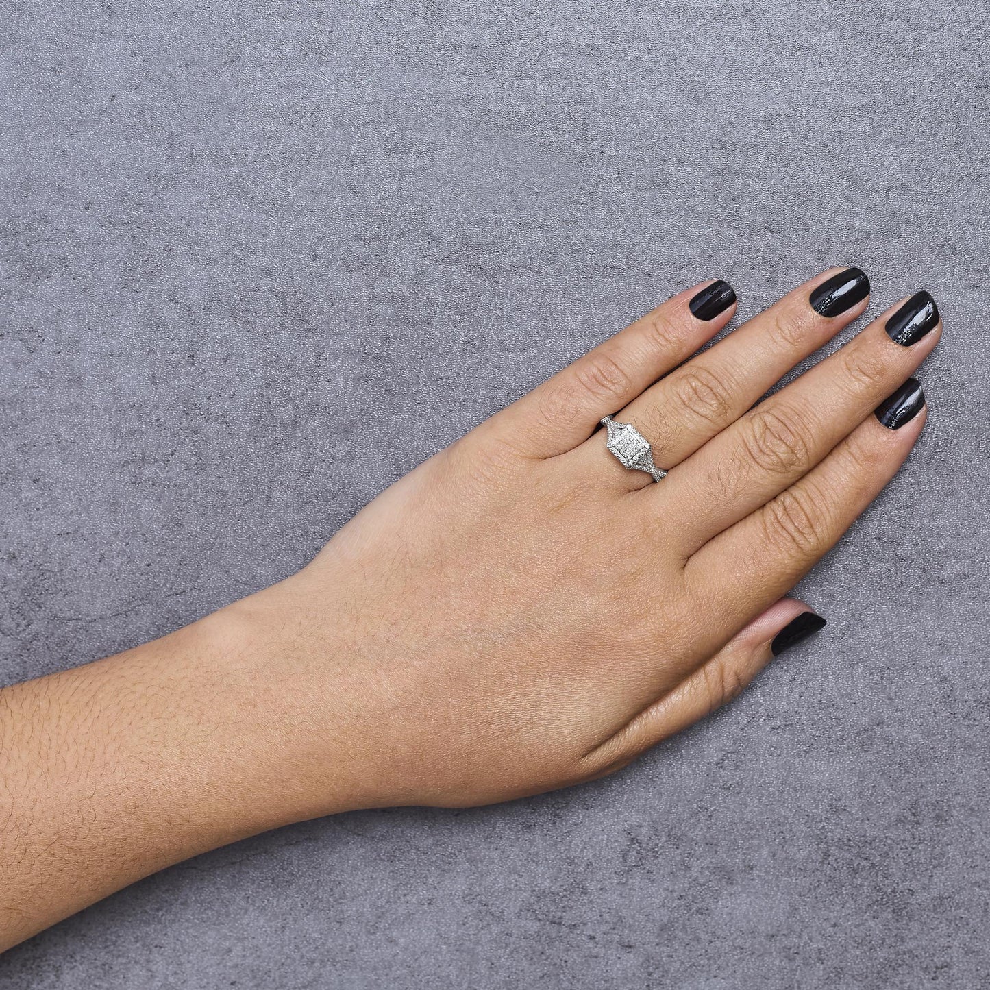 White metal ring with princess-shaped white gemstones in an invisible setting, worn on a model's hand, top-down angle.