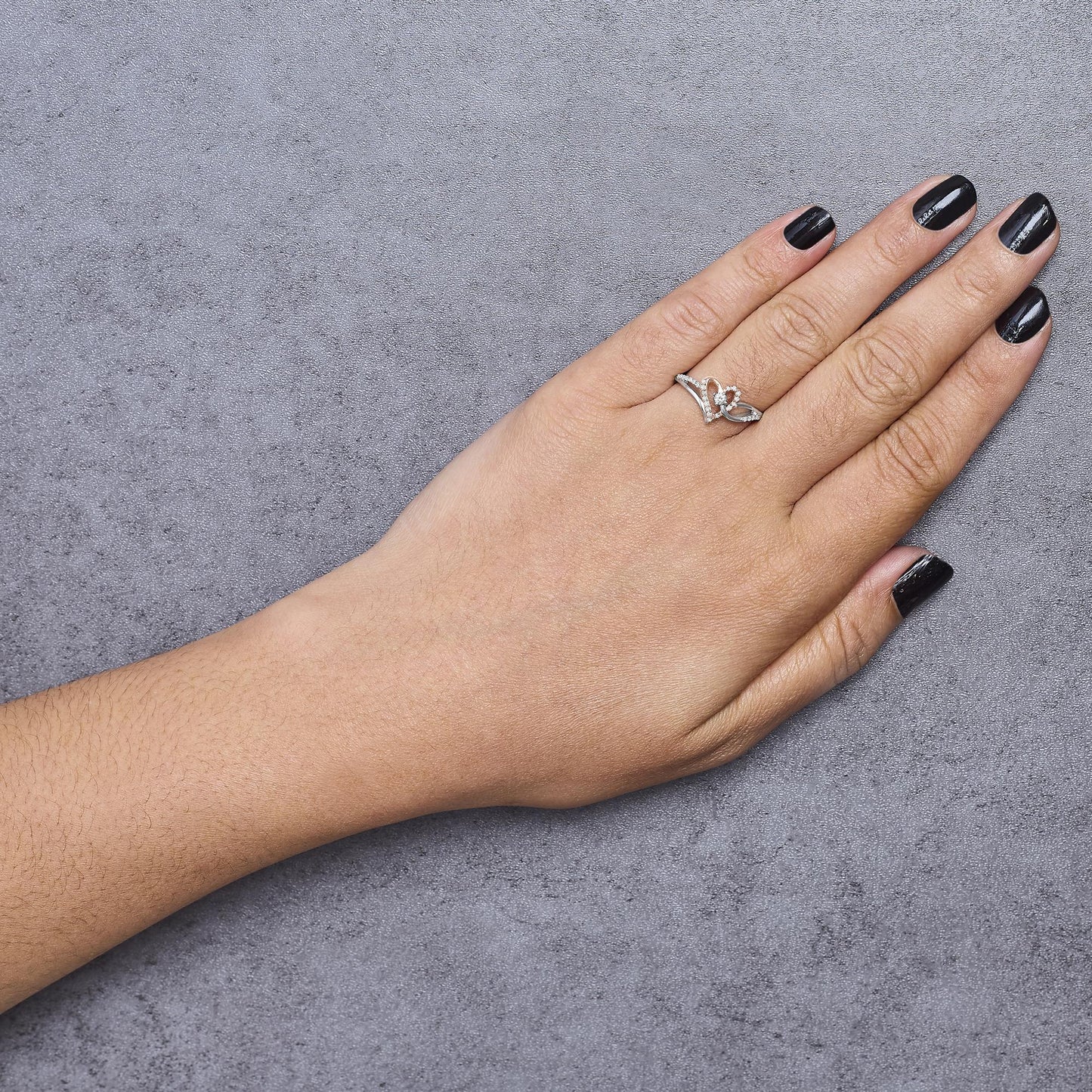 Hand wearing a white and rose metal ring with round white gemstones in prong settings, shown from above.