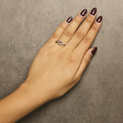 Rose-colored ring with white round gemstones in prong settings forming a heart shape, shown on a model's hand from above.