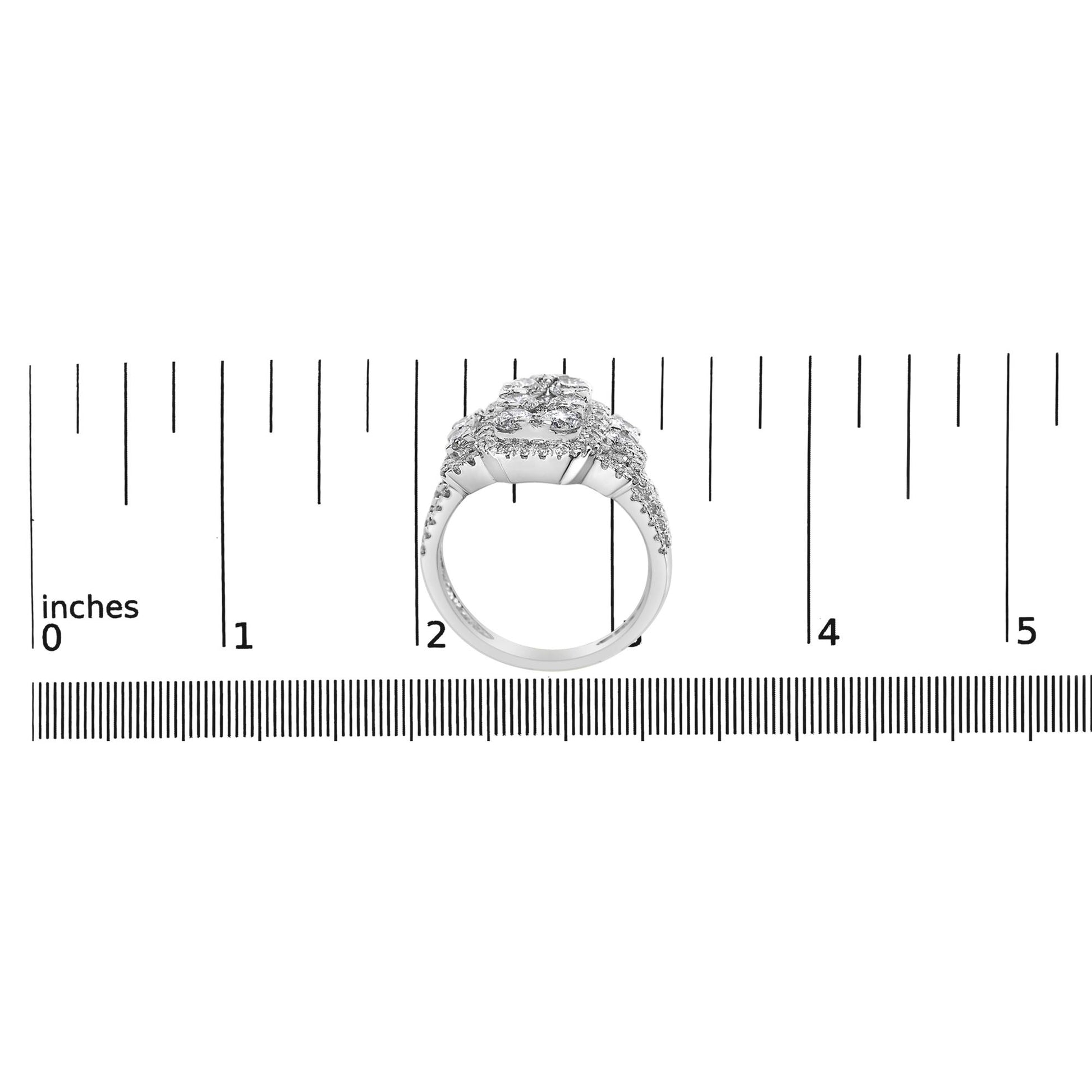White metal ring with multiple prong-set white round gemstones viewed from the front, positioned on a ruler for size reference.