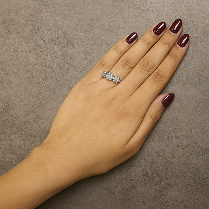 White metal ring with three clusters of round white gemstones in prong settings, shown on a model’s hand from above.