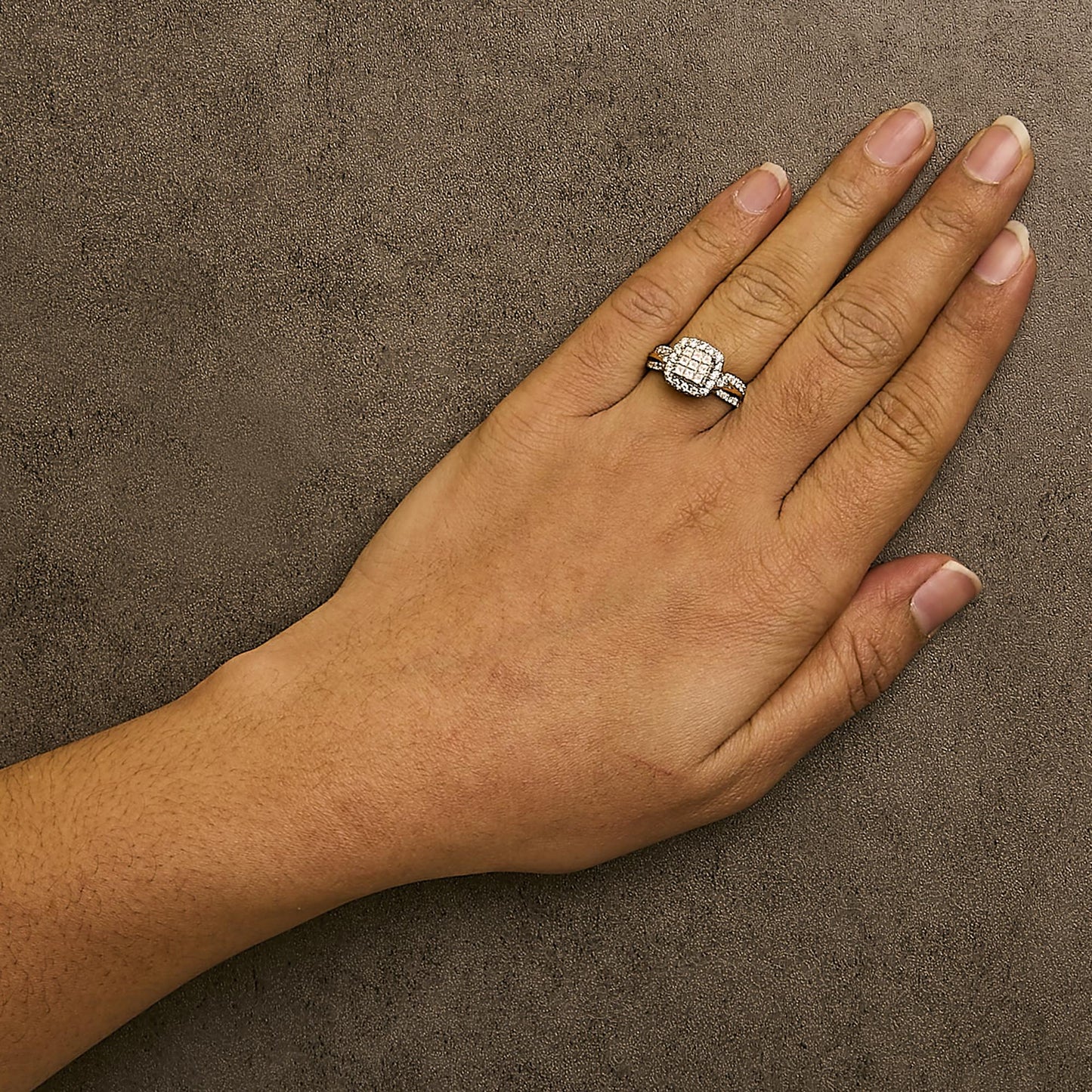 Close-up shot of a yellow metal ring with multiple white gemstones in round pave and princess invisible settings, worn on a model's hand.