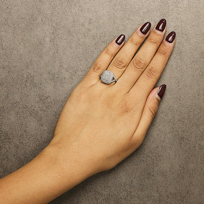 Close-up of a white metal ring with multiple white gemstones in prong settings, worn on a model's left hand, shot from above.