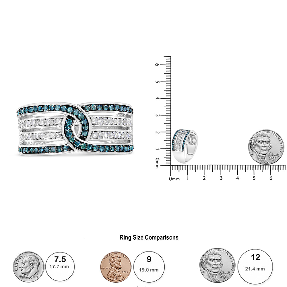 Close-up front view of a white metal ring featuring alternating rows of round white and blue pave-set gemstones with an overlapping knot design, shown next to a ruler and coin for size reference.