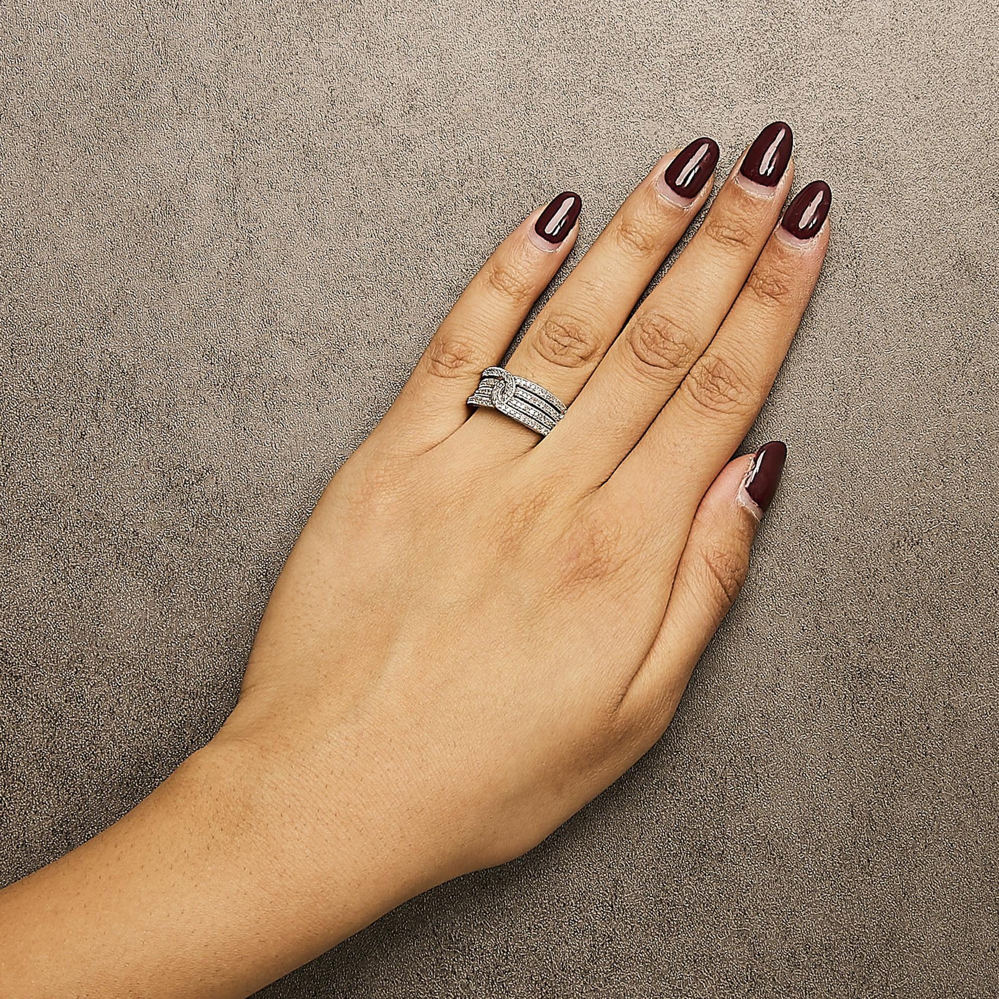 Top view of a hand wearing a white metal ring featuring multiple bands adorned with round white gemstones in shared prong settings.