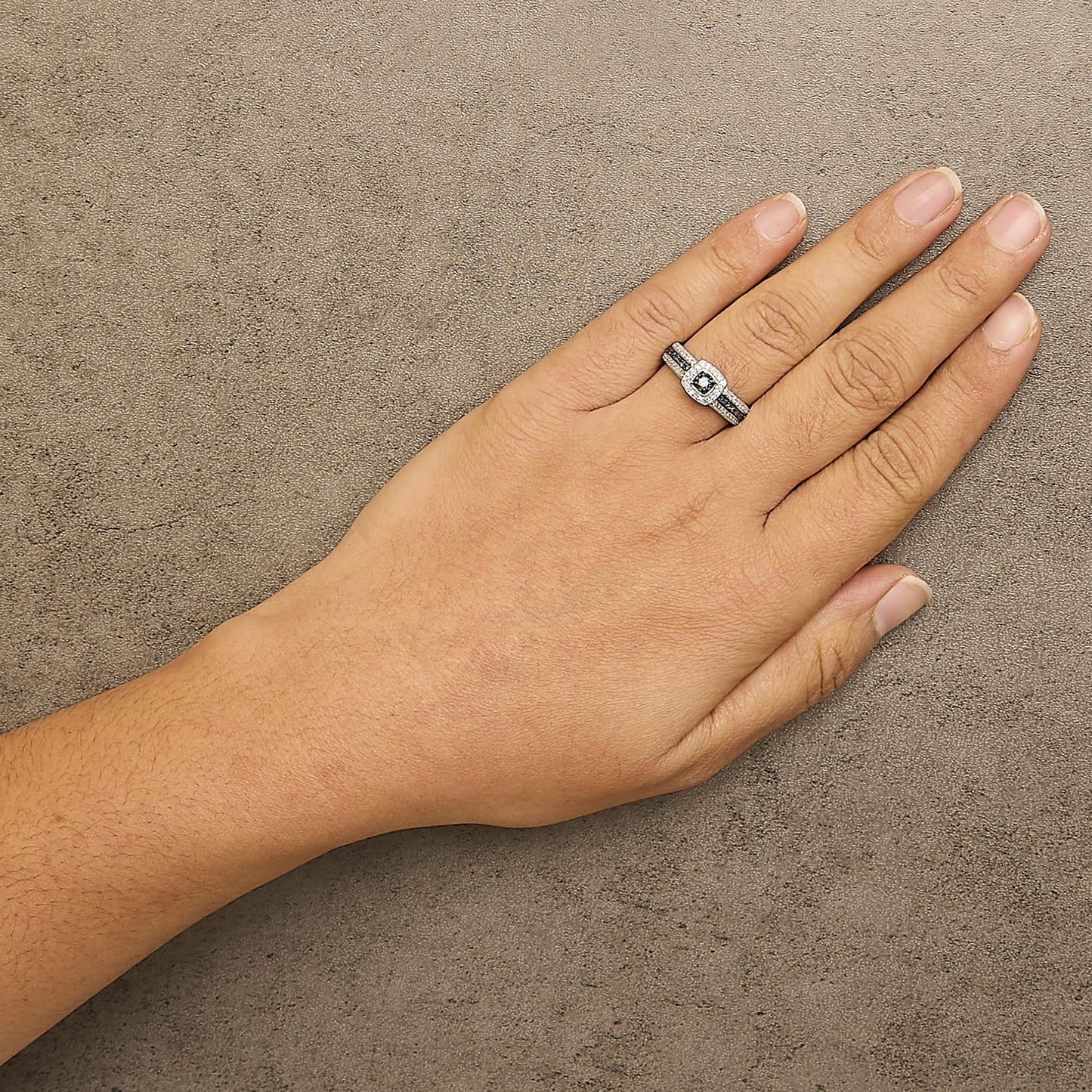 White metal ring with a central blue gemstone surrounded by blue and white gemstones in a prong setting, worn on a hand, shown from above at an angle.