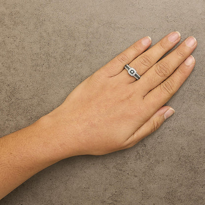 White metal ring with a central blue gemstone surrounded by blue and white gemstones in a prong setting, worn on a hand, shown from above at an angle.